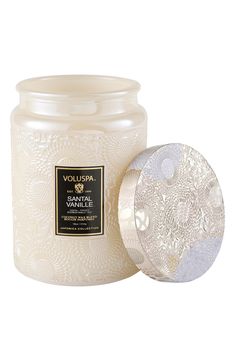 a white candle with an intricate design on the lid and inside, next to it's glass container