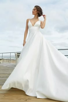 a woman in a white wedding dress standing on a wooden deck next to the ocean