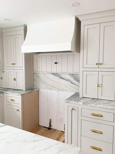 a white kitchen with marble counter tops and gold pulls on the cabinet doors is shown