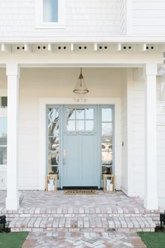 a blue front door on the side of a white house with brick walkway and grass