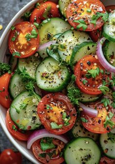 a white bowl filled with cucumbers, tomatoes and onions on top of a table