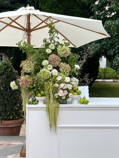 an umbrella is set up on top of a table with flowers and fruit in vases