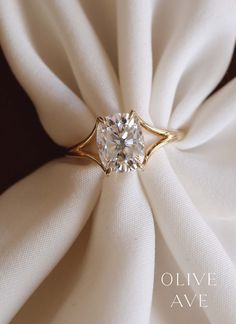 a diamond ring sitting on top of a white cloth covered napkin with the words olive ave written below it