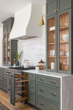 a kitchen with green cabinets and marble counter tops, gold pulls on the oven hood