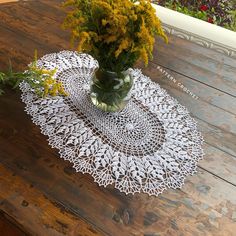 a vase filled with yellow flowers sitting on top of a wooden table covered in white doily