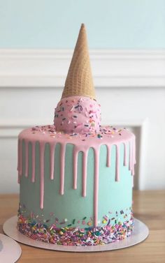 a birthday cake with sprinkles and an ice cream cone on top is sitting on a table