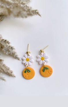 the earrings are decorated with white flowers and green leaves on top of an orange slice