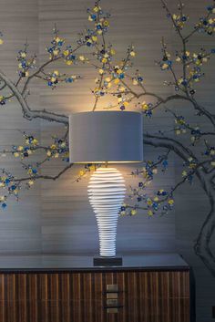 a lamp that is next to a tree with blue and yellow flowers on it in front of a wall