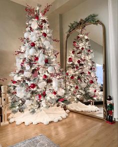 a white christmas tree with red and silver ornaments in front of a mirror on the floor