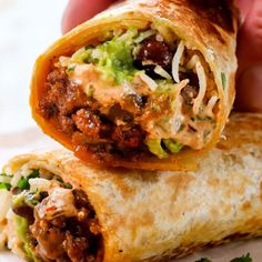 a hand holding a burrito filled with meat and veggies