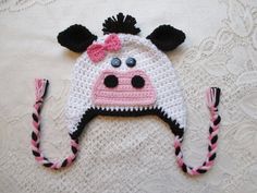 a crocheted cow hat with black ears and pink nose is laying on a white surface