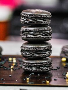 a stack of black macaroons sitting on top of a wooden table next to gold flecks