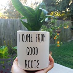 a hand holding a coffee mug with a plant in it that says i come from good roots