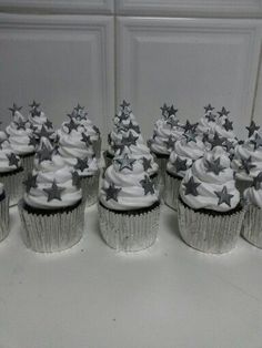 cupcakes with white frosting and silver stars on top are lined up in rows