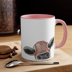 a pink and white coffee mug with a cow's face painted on the side