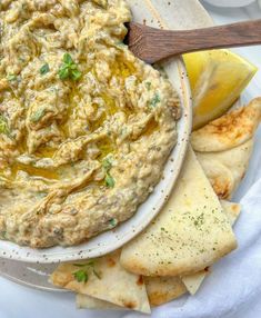 hummus and pita chips on a plate with a wooden spoon next to it