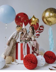 two children sitting on top of a red and white box surrounded by balloons, confetti and streamers