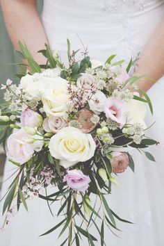 a bridal holding a bouquet of white and pink flowers with greenery on it