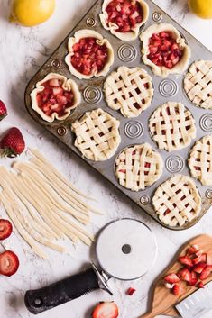 fresh strawberries and pies on a baking sheet next to a knife, lemons, and other ingredients