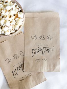 two brown paper bags filled with popcorn next to a bowl of popcorn on top of a table