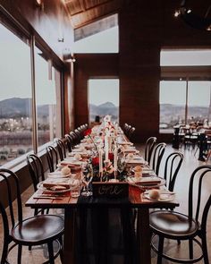 a long table set up with place settings and candles on it in front of large windows