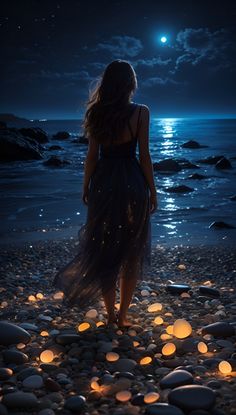 a woman standing on the beach at night with her back to the camera, looking out over the water