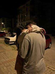 two people hugging each other on the side of a road at night with cars in the background