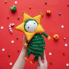 a hand holding a small stuffed toy with a star on it's head and green pine cone