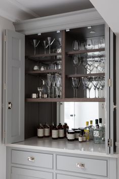 an open cabinet filled with wine glasses and liquor bottles on top of a white counter