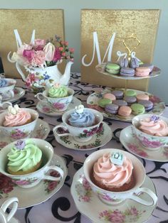 there are many cupcakes on the table with teacups and saucers