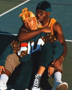 a man and woman sitting on top of a tennis court holding each other's arms