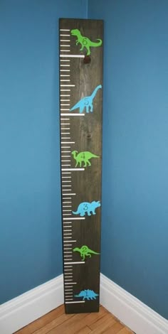 a wooden ruler with dinosaurs on it in the corner of a blue room, next to a wall