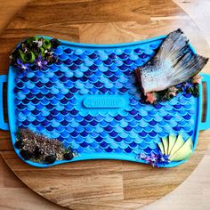 a fish is laying on top of a blue tray with plants and other things in it