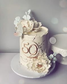 a white cake with flowers and the number 50 on it sitting next to a plate