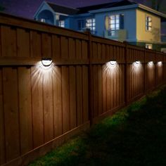 three lights on the side of a wooden fence at night with houses in the background