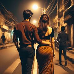 two people are walking down the street at night, one is wearing a brown sari