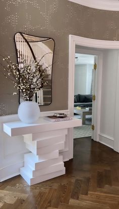 a white table with a vase on top of it next to a mirror and door