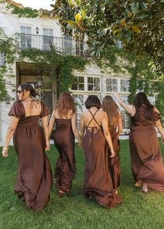 four women in brown dresses are walking through the grass