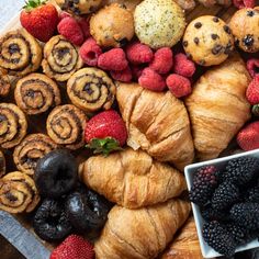 an assortment of pastries and berries are arranged on a platter, including croissants