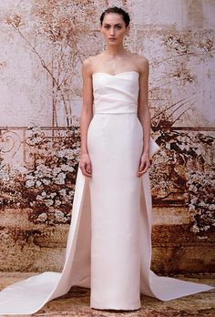 a woman standing in front of a wall wearing a white dress