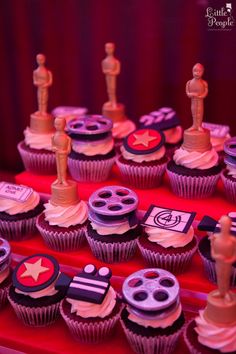 cupcakes with decorations on them are displayed in front of a red curtain and drapes