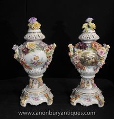 two white vases with flowers on them sitting side by side in front of a black background