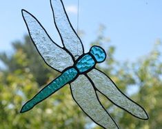 a stained glass dragon sitting on top of a window sill with trees in the background