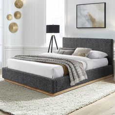 a bedroom with white walls and wood flooring has a gray upholstered bed