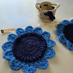 two crocheted blue flowers are next to a measuring tape on a white table