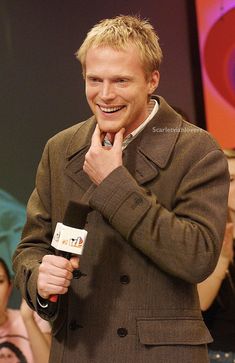 a man with blonde hair is holding a microphone and smiling at the camera while standing in front of an audience