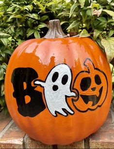 an orange pumpkin with black letters and ghost faces painted on it, sitting in front of some bushes