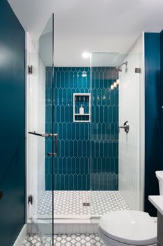 a white toilet sitting next to a walk in shower under a blue tiled bathroom wall