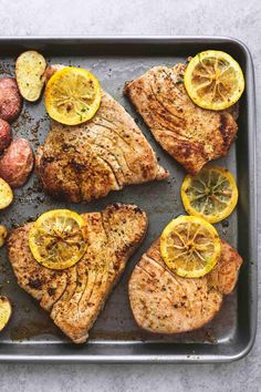 a pan with meat, potatoes and lemons on it