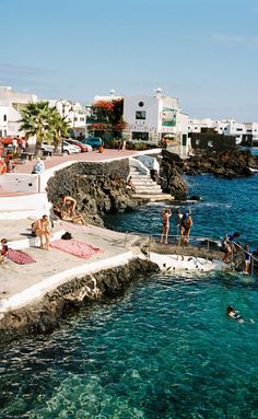 people are swimming in the blue water near some buildings